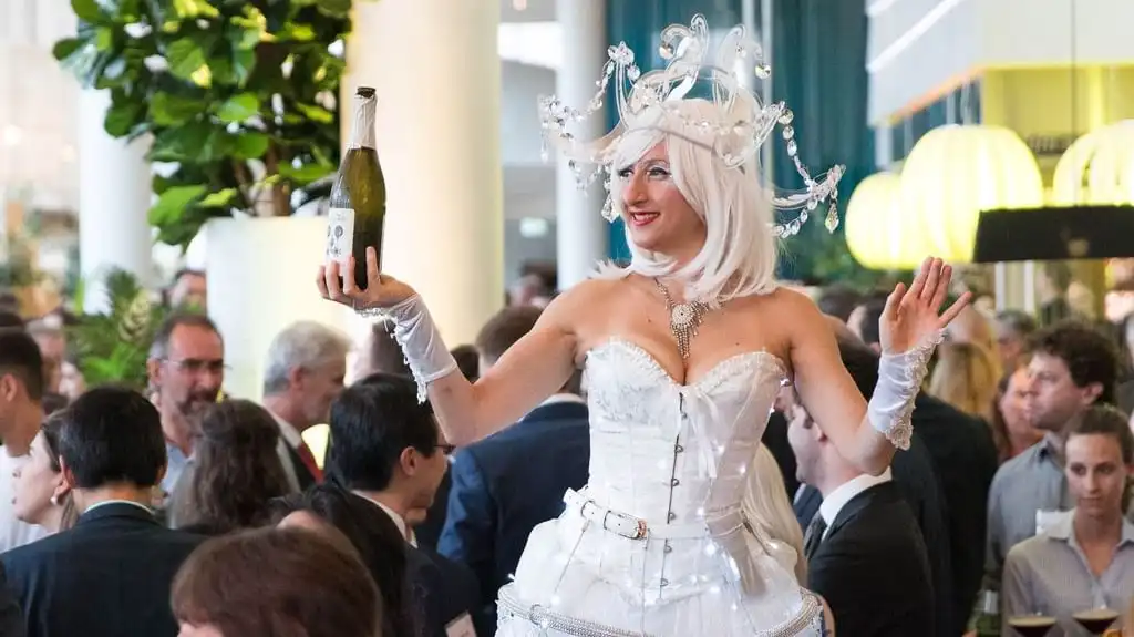 Performer in white costume serving champagne at a lively corporate event