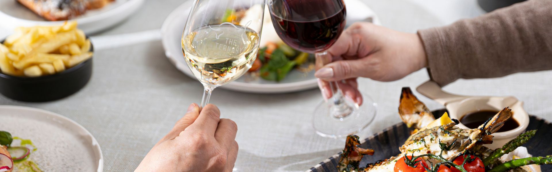 Diners toasting with wine over seafood dishes at Ternary Restaurant