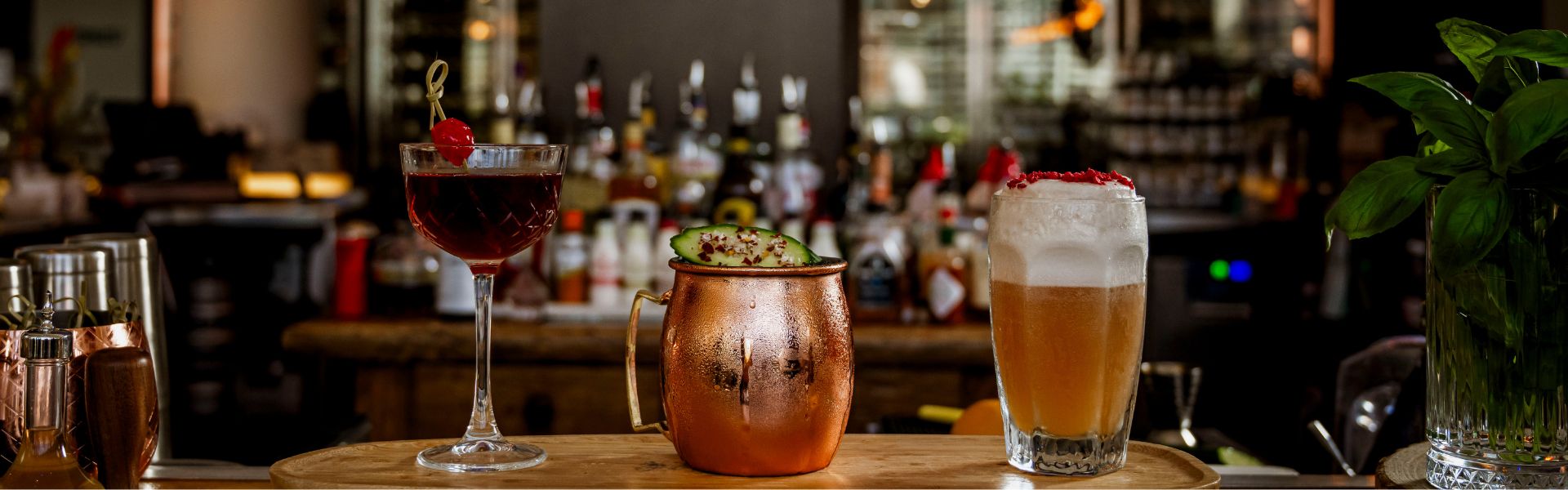 Selection of cocktails and drinks on a bar at happy hour at Ternary Restaurant, including a cherry cocktail, Moscow mule, and beer.